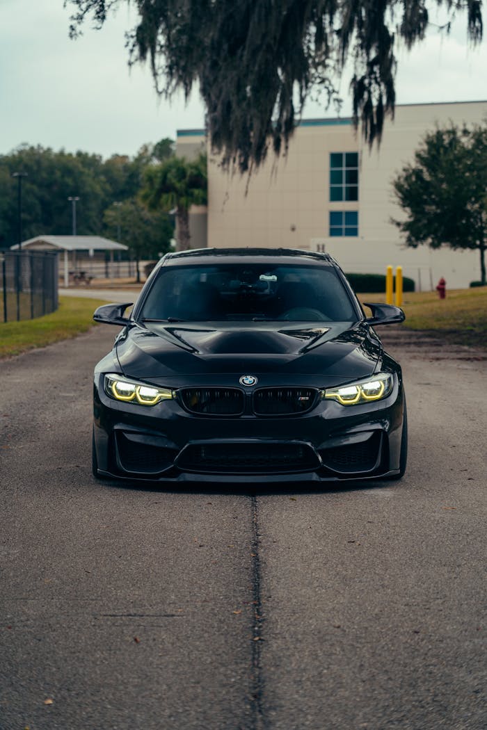 A modern black car parked on an outdoor road in a quiet setting, surrounded by greenery.